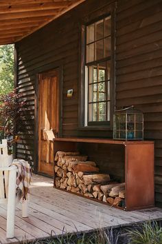 a wooden porch with firewood stacked on it and a table in front of the door