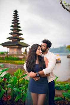 a man and woman standing next to each other in front of a body of water