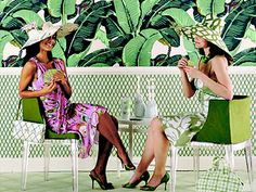 two women sitting on green chairs in front of a wall with large leaves and palm trees