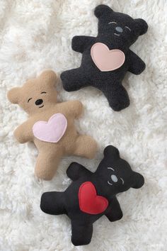 three teddy bears with hearts on them laying on a white blanket, one is black and the other is brown