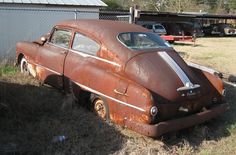 an old rusted out car sitting in the grass next to a fence and building