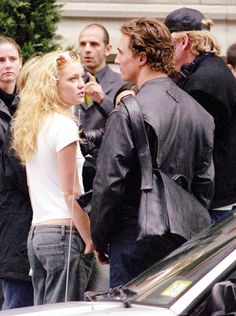 a group of people standing next to each other near a car and police officer in the background