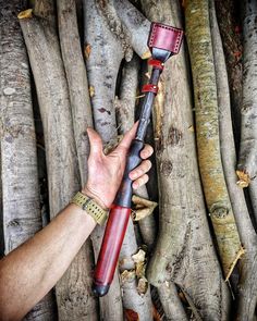 a hand holding a red and black blow dryer in front of some tree trunks