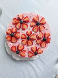 there is a cake with strawberries and blueberries on the top, sitting on a white table cloth