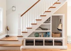 there is a book shelf under the stairs in this house with baskets and shoes on it