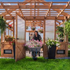 a woman sitting in a wheelbarrow filled with potted flowers next to a wooden structure