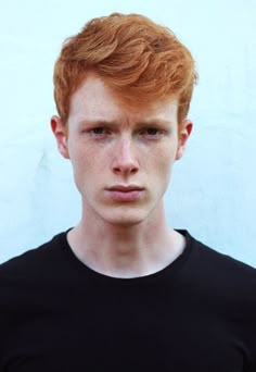 a young man with red hair wearing a black t - shirt and looking at the camera