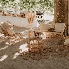 an outdoor seating area with wicker chairs and pillows on the ground under a tree