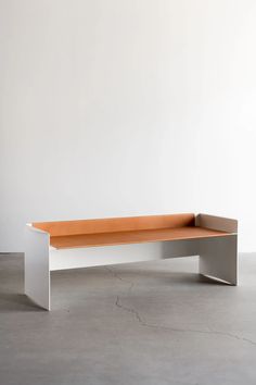 an orange and white bench sitting on top of a cement floor next to a wall