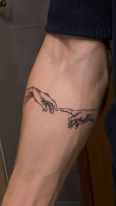 the creation of man's hands tattoo on the left arm and right hand behind him