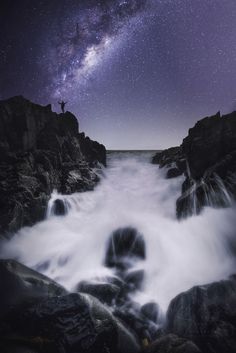 a man standing on top of a rocky cliff under a night sky filled with stars