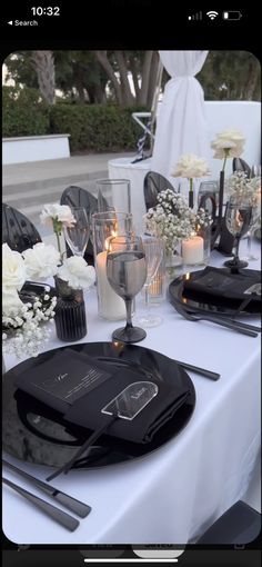 the table is set with black and white flowers in vases, silverware, and candles