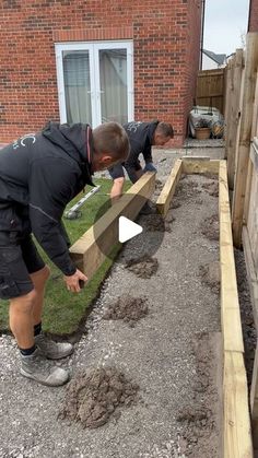 two men are working in the yard with some grass and dirt on the side of a building