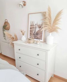 a white dresser sitting in a bedroom next to a wall with pictures and plants on it