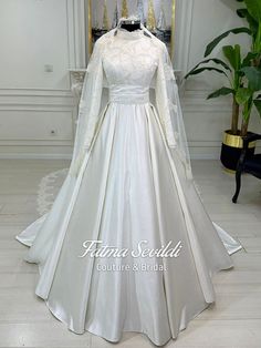 a white wedding gown with long sleeves and lace on the top, in front of a mirror