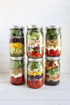 four mason jars filled with different types of salads and vegetables, all lined up on top of each other