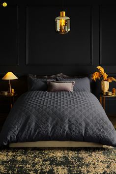 a bedroom with black walls and a bed covered in grey blankets, pillows and throw pillows