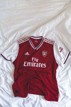 a red and white soccer jersey laying on top of a bed next to a pillow