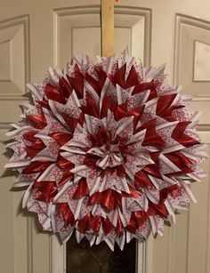 a red and white wreath hanging from the front door with ribbon on it's side