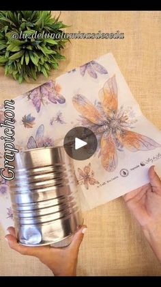 a person holding a tin can with butterflies on it next to some papers and a potted plant