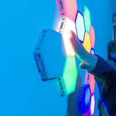 a person holding an electronic device in front of a colorful light display on the wall