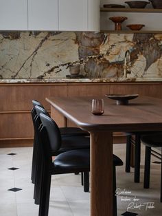 a wooden table sitting in the middle of a kitchen with black chairs and marble counter tops