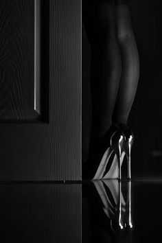 black and white photograph of woman's legs with high heeled shoes in front of door