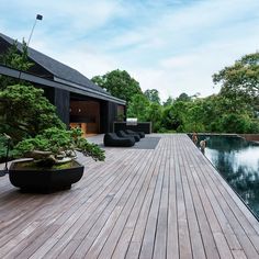 a wooden deck next to a large pool with trees in the foreground and an outdoor lounge area on the other side