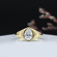 a yellow gold ring with a pear shaped diamond in the center on a white surface