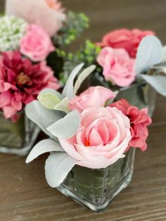 three small vases with flowers in them sitting on a wooden table, one is pink and the other is green