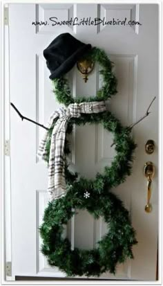 a snowman made out of wreaths hanging on a door with a black hat