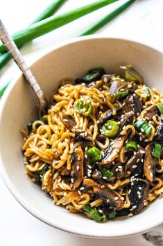 a white bowl filled with noodles and vegetables on top of a table next to chopsticks