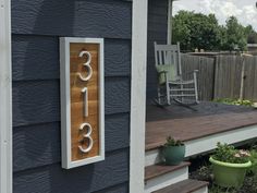 a wooden house number sign mounted to the side of a blue wall next to a porch