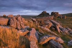 some rocks and grass on a hill under a cloudy sky