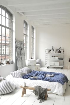 an unmade bed sitting in the middle of a room next to two large windows