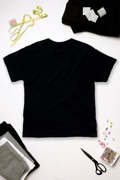 black t - shirt and accessories laid out on top of the table with scissors, thread, paper clips, and other items