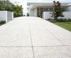 an empty driveway in front of a house with white fence and trees on both sides