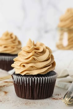 two cupcakes with frosting sitting on top of a white table next to utensils