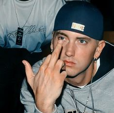 a young man wearing a hat and holding his hand up to his face while sitting next to another person