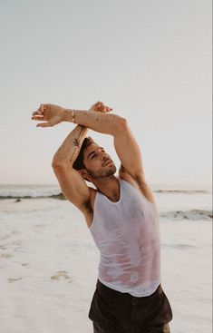 a man standing on top of a beach next to the ocean holding his arm up