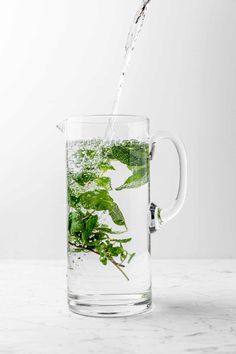 water being poured into a glass mug filled with green leaves