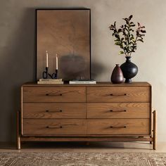 a wooden dresser with two vases on top of it next to a painting and candles