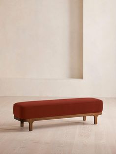 a red bench sitting on top of a hard wood floor next to a white wall