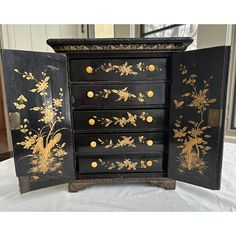 an old black and gold painted dresser with drawers on it's sides, in front of a window