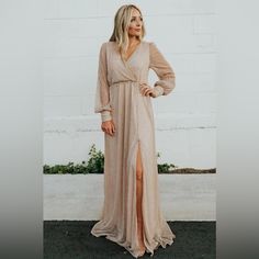 a woman standing in front of a white brick wall wearing a long dress and heels