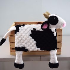 a crocheted black and white cow laying on top of a wooden pallet