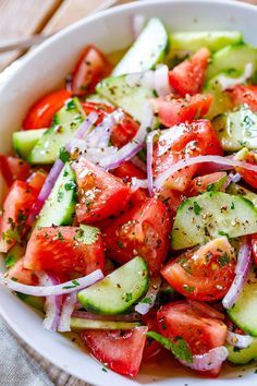 a white bowl filled with cucumber, tomato and onion salad on top of a table