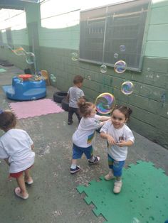 three young children playing with soap bubbles in an indoor play area at the school building