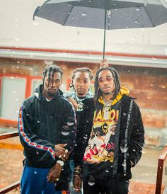 three men standing under an umbrella in the rain