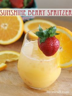 a close up of a drink on a table with oranges and strawberries in the background